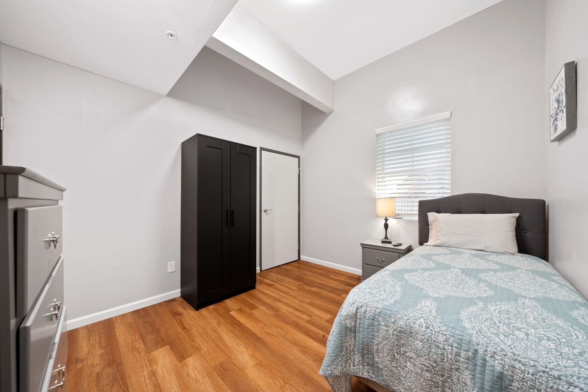 A modern bedroom with a bed, black wardrobe, and a lamp on a nightstand.