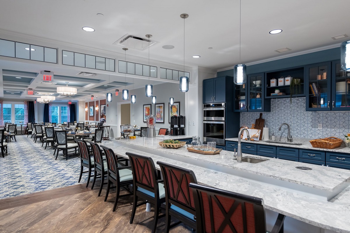 A modern kitchen interior with a long countertop and bar stools, featuring pendant lighting.