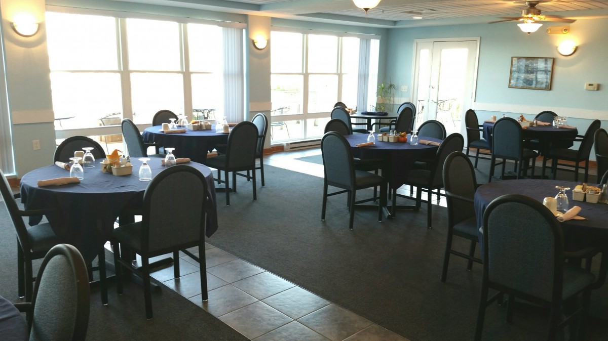 A cozy dining area with neatly arranged tables and chairs, illuminated by large windows.