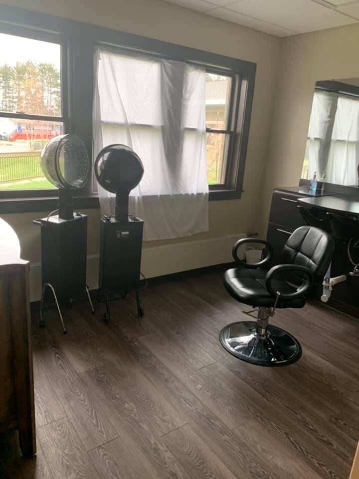 A hair salon with a styling chair and two dryers by the window.