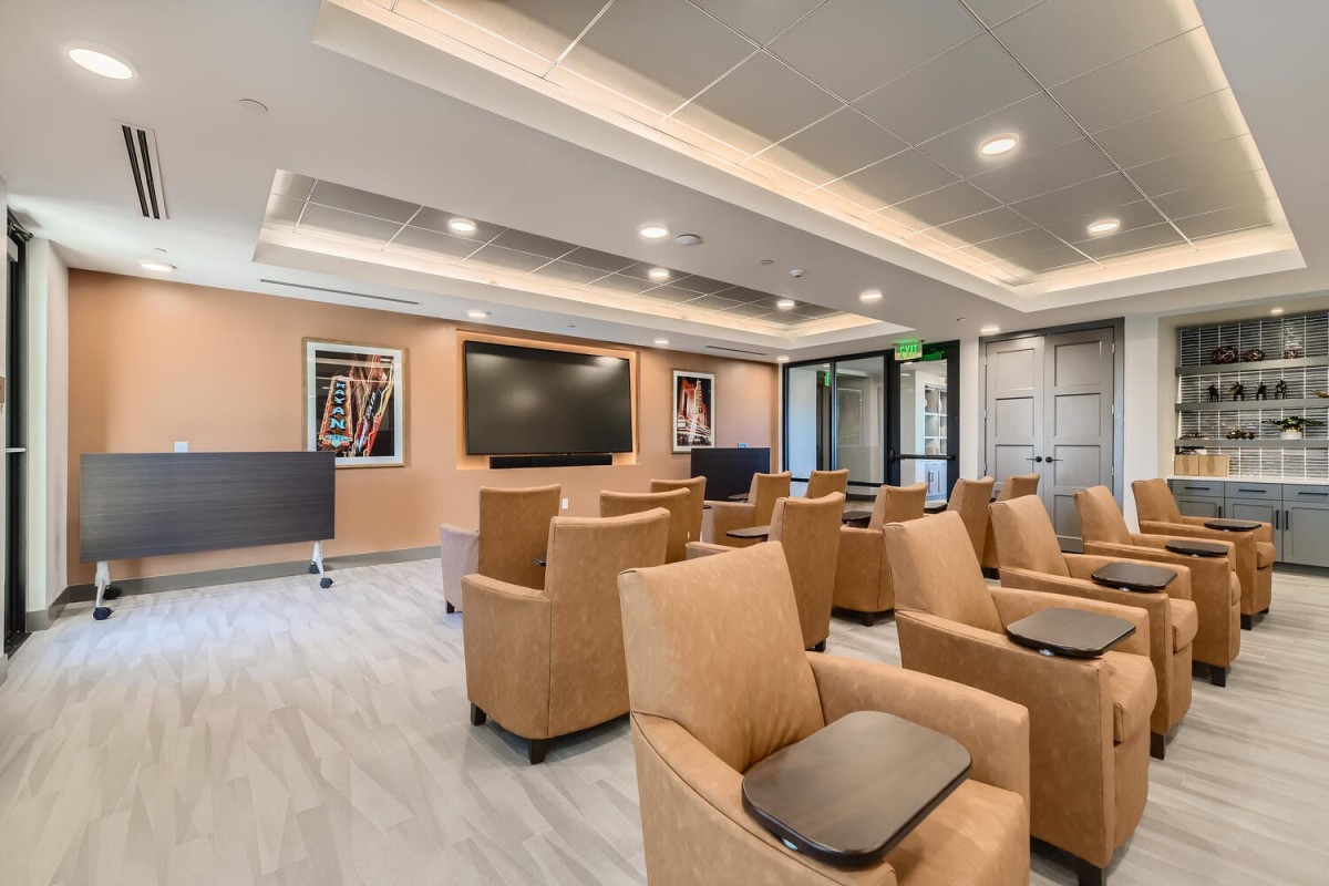 A modern lounge with comfortable seating and a large screen, suitable for meetings or presentations.