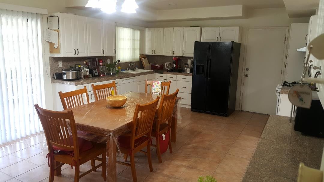 A spacious kitchen with a wooden dining table and chairs, featuring white cabinets and a black refrigerator.