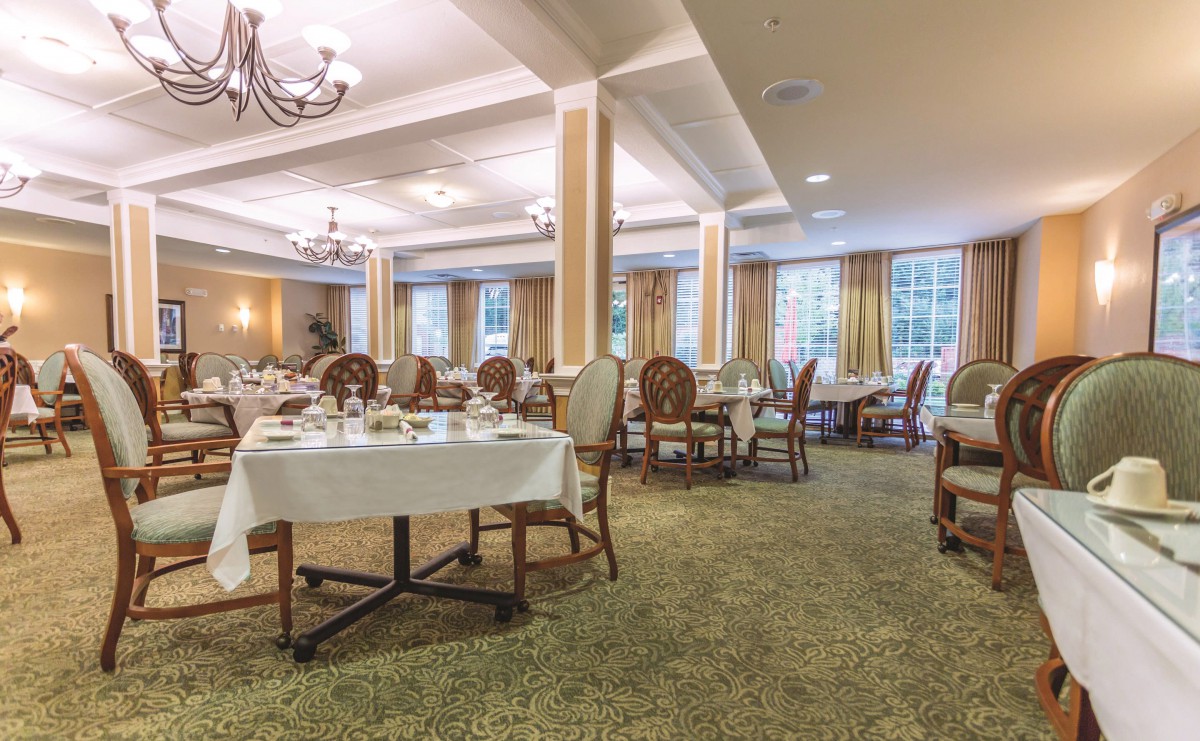 An elegant dining room with neatly arranged tables and chairs, illuminated by chandeliers.