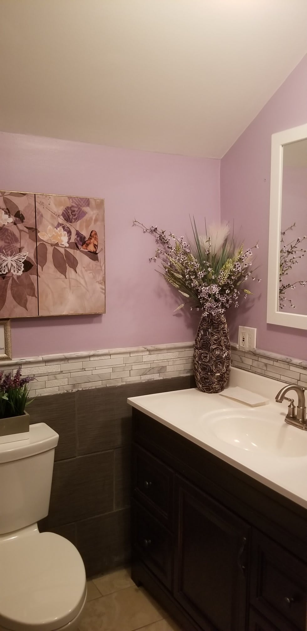 A stylish bathroom with lavender walls, featuring floral artwork and a decorative vase.
