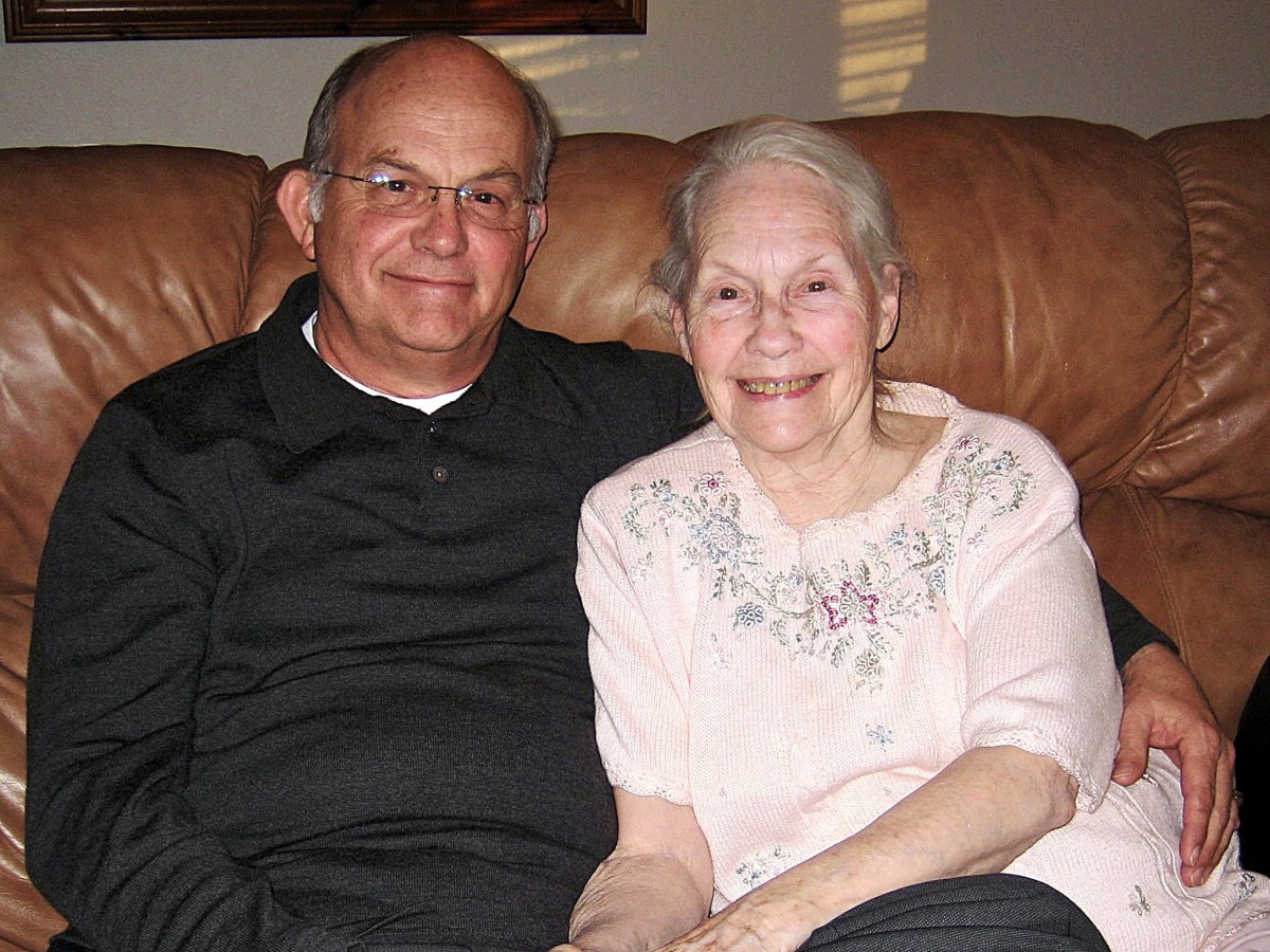 An elderly couple sitting on a sofa, smiling warmly at the camera.