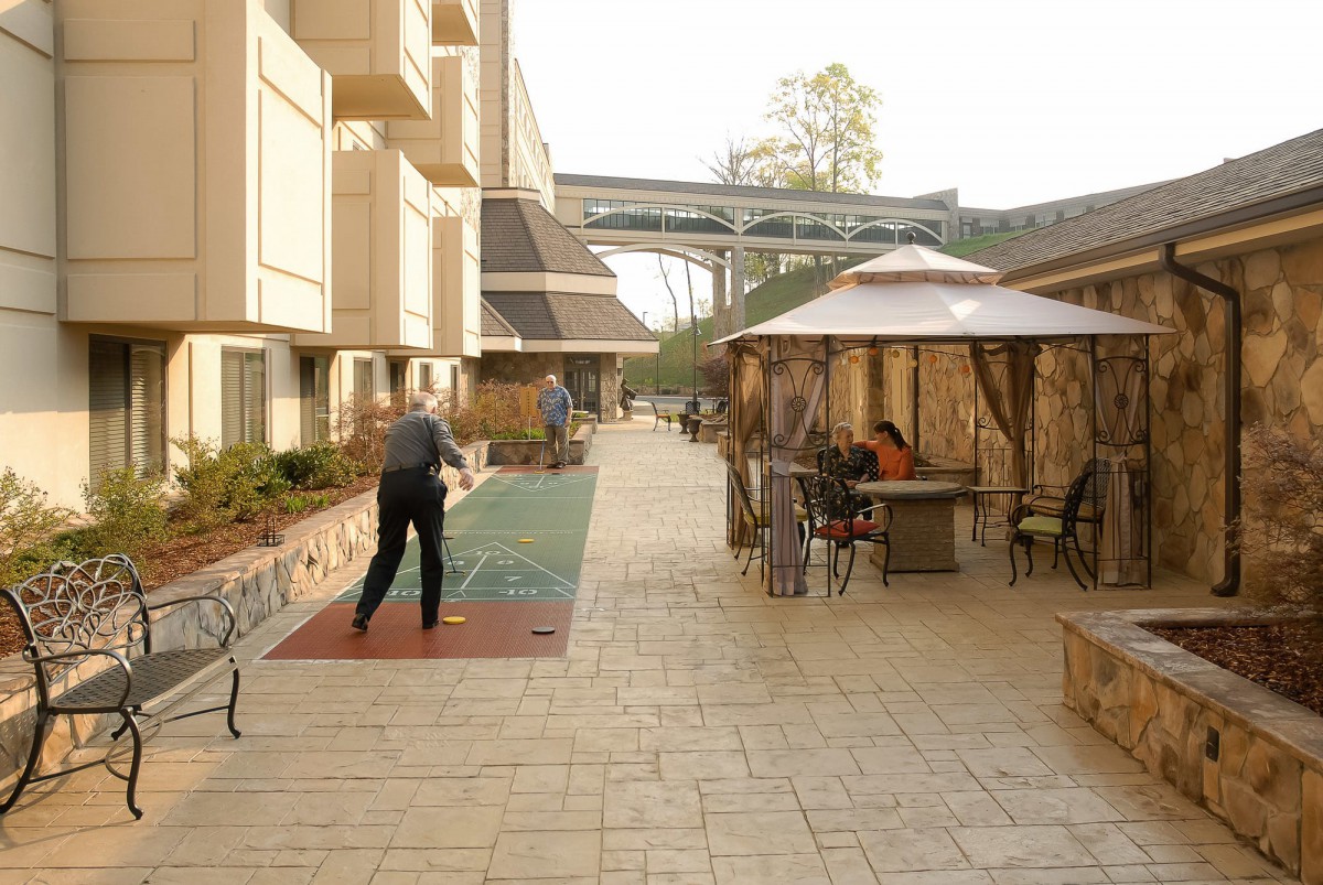 An outdoor courtyard with people sitting at tables and playing shuffleboard.