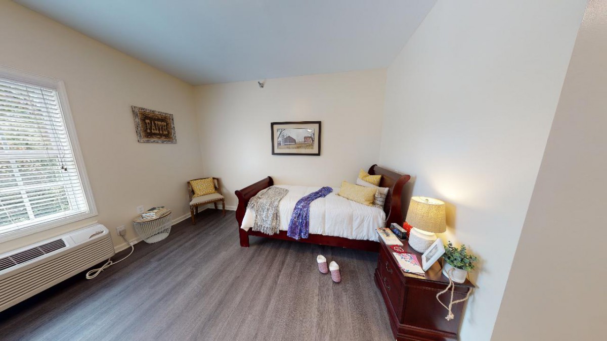 A cozy bedroom with a single bed, nightstand, and warm lighting.