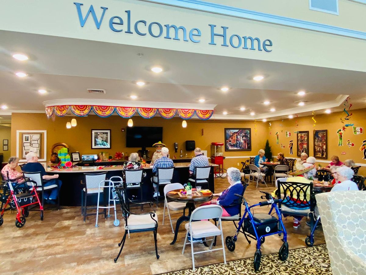 A welcoming community space with people seated at tables, featuring a 'Welcome Home' sign.