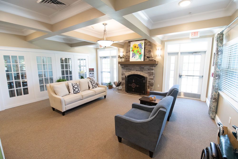A cozy living room with sofas facing a stone fireplace, decorated with artwork and illuminated by natural light from large windows.