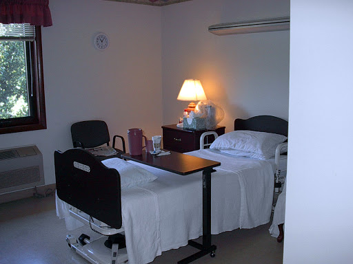 A hospital patient room featuring two beds, a lamp, and a small table.