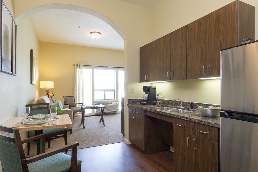 A cozy apartment interior featuring a kitchenette with wooden cabinets and a connected living room area.