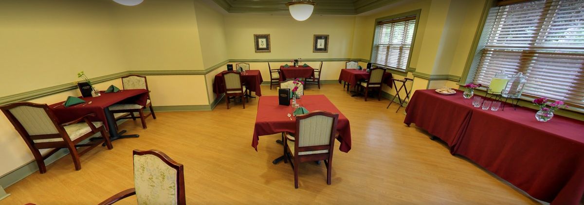 An empty dining room with tables covered in red tablecloths.