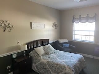 A cozy bedroom with a wooden bed, patterned bedding, a chair by the window, and simple decor.