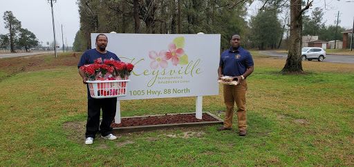 Two men standing in front of a sign displaying the name and address of a flower shop.