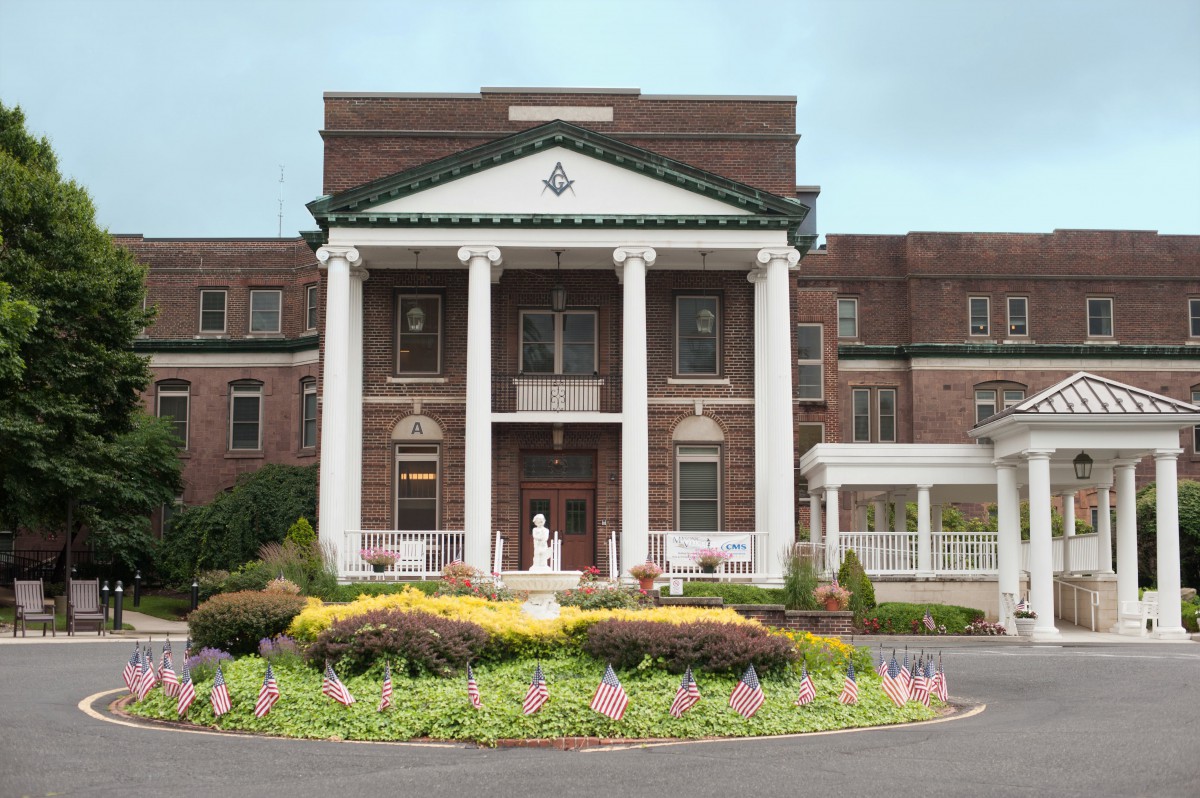 A grand building with large white columns and well-maintained gardens at the entrance.