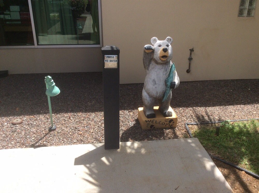 A bear statue stands on a sidewalk next to a tall black post on a sunny day.