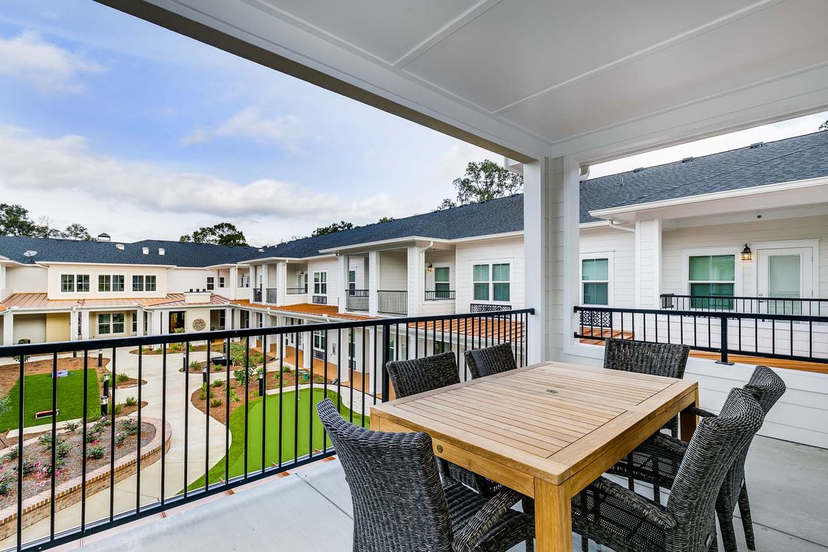A modern apartment balcony with a wooden dining set overlooking the courtyard.