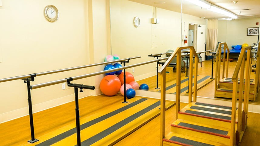 A physical therapy room with parallel bars and exercise balls.