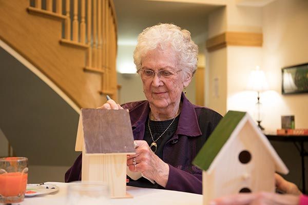 An elderly woman is crafting a birdhouse indoors, focusing on her hobby.