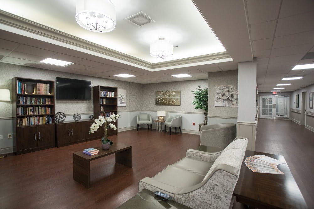 A modern waiting room with comfortable sofas, artwork, and a bookshelf, featuring wooden floors and elegant lighting.