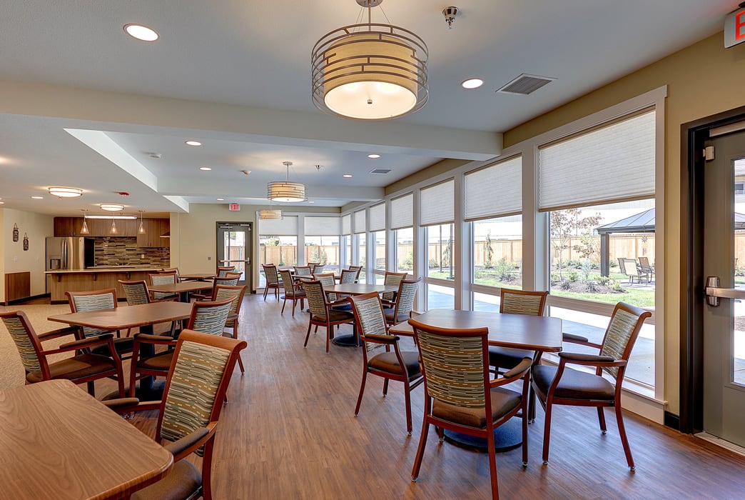 A spacious dining area with multiple tables and chairs, illuminated by ceiling lights.