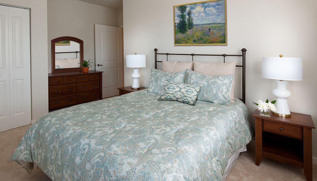 A cozy bedroom with a neatly made bed and decorative pillows, a bedside lamp, and a painting on the wall.