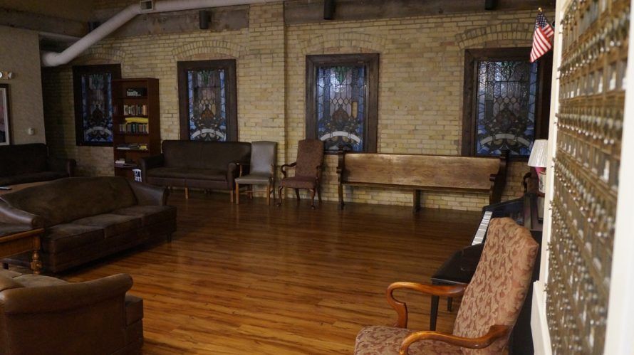 A cozy room with wooden flooring, brick walls, and various chairs arranged around the space.
