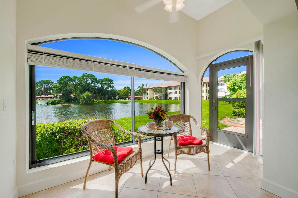 A bright sunroom with a beautiful lake view, featuring cozy seating and vibrant decor.