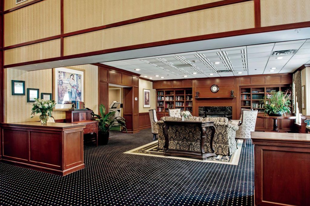 A cozy library interior with bookshelves, a central table surrounded by chairs, and warm wooden decor.