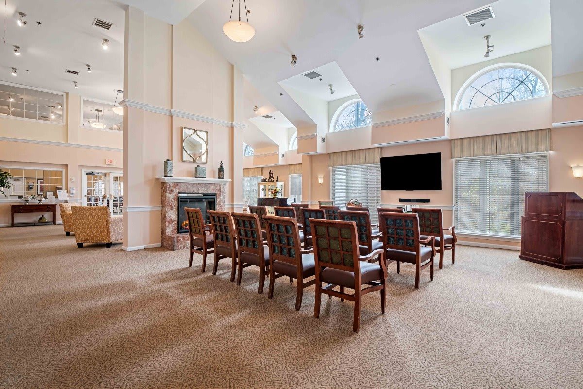 A spacious meeting room with rows of chairs facing a large television and a fireplace.