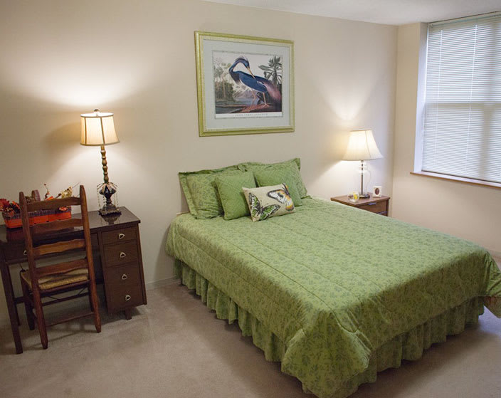 A cozy bedroom with green bedding, two nightstands with lamps, and a painting on the wall.