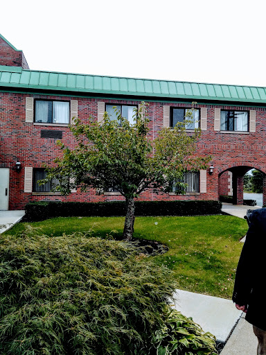 A brick building with a green roof, surrounded by well-maintained landscaping and a tree.