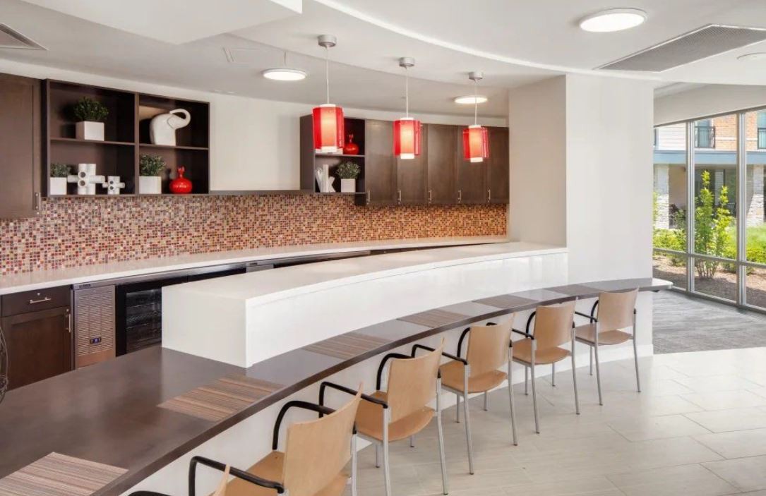 A sleek, modern kitchen with a curved counter and wooden chairs under vibrant red pendant lights.