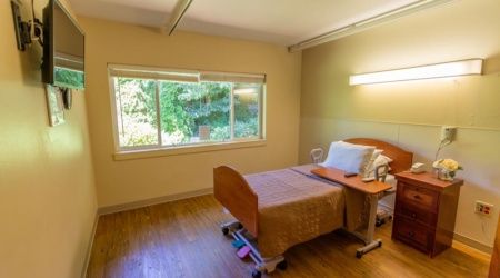 A minimalist hospital room with a single bed and a large window allowing natural light to fill the space.