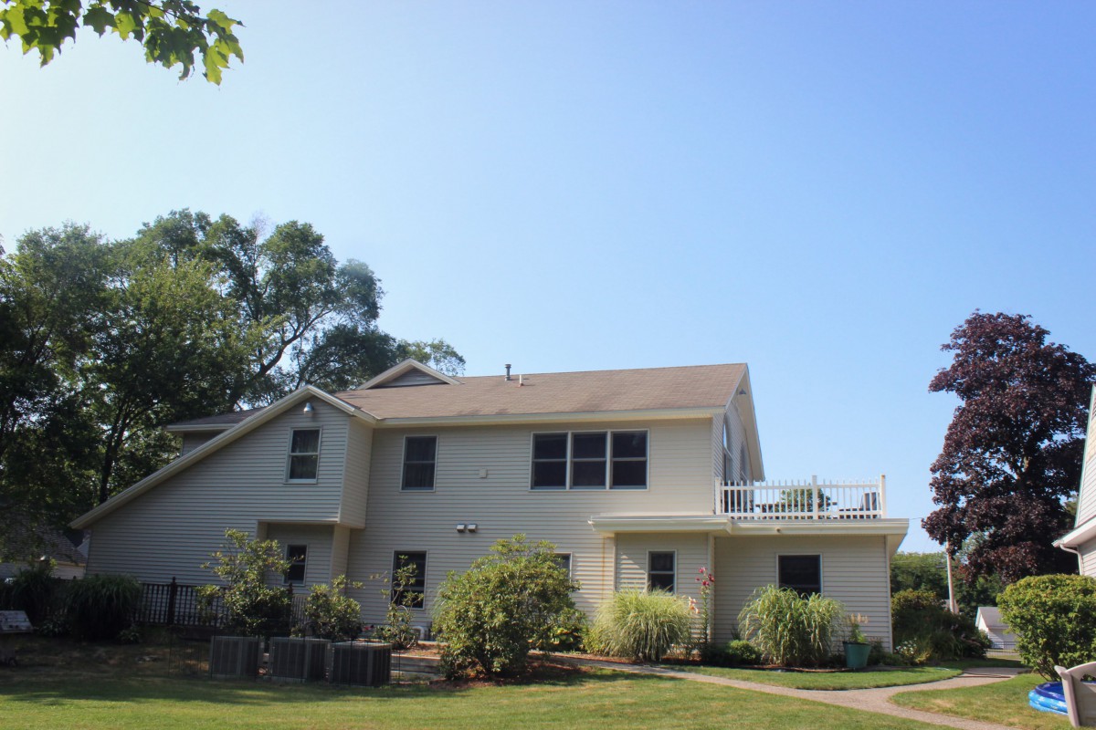 A two-story house surrounded by a garden with trees under a clear blue sky.