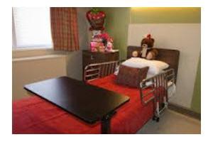 A hospital room with a decorated bed and a table, featuring flowers and gifts.
