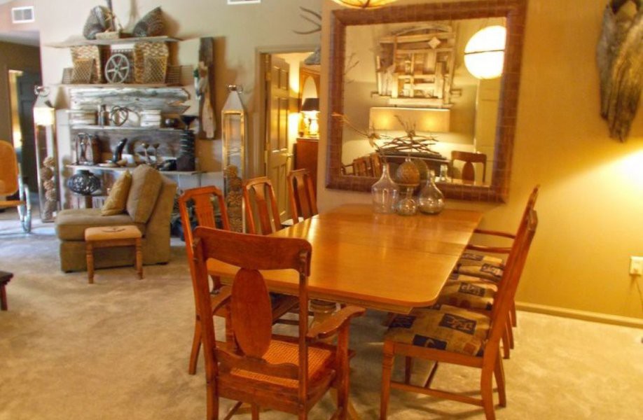 A cozy dining room with a large wooden table, surrounded by chairs and adorned with a decorative mirror on the wall.