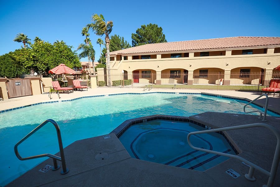 A sunny day at a resort featuring an outdoor swimming pool and hot tub surrounded by palm trees.