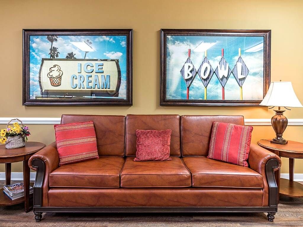 A cozy leather couch adorned with red pillows is set against a backdrop of colorful wall art featuring ice cream and bowling themes.