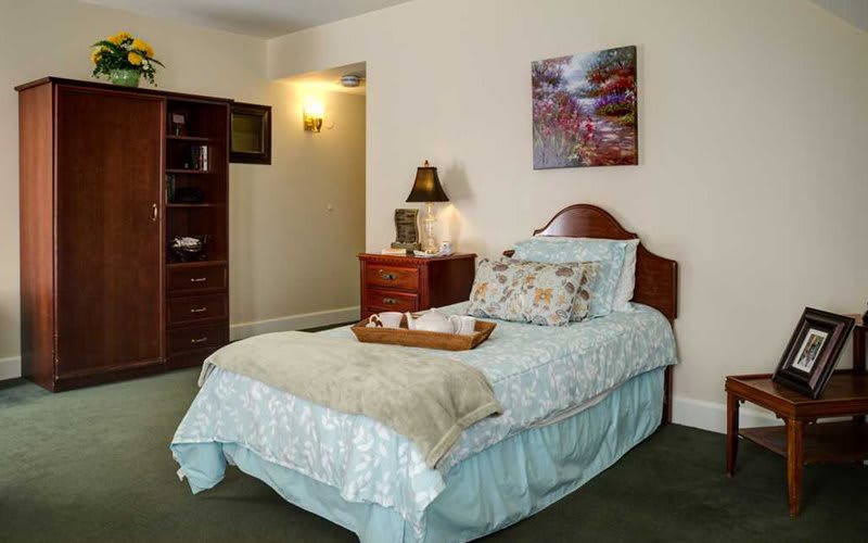 A cozy bedroom with a neatly made bed, decorative pillows, and a nightstand with a lamp and artwork on the wall.