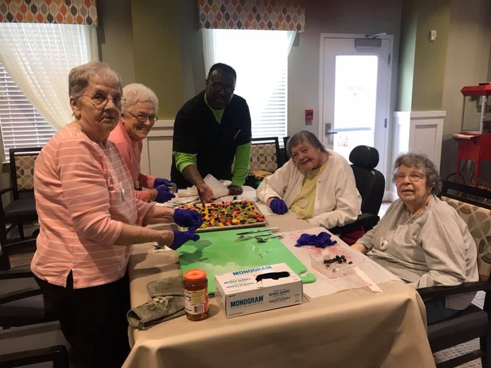 A group of seniors enjoying a cooking activity together indoors, smiling and engaged.