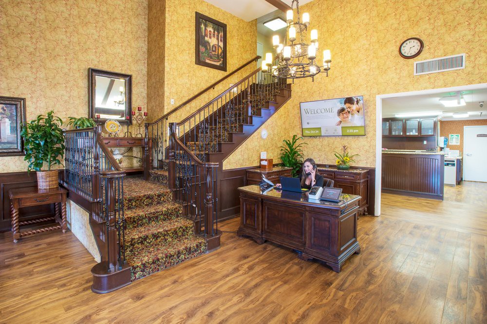 A warmly decorated office lobby featuring a wooden reception desk, ornate staircase, and chandelier.