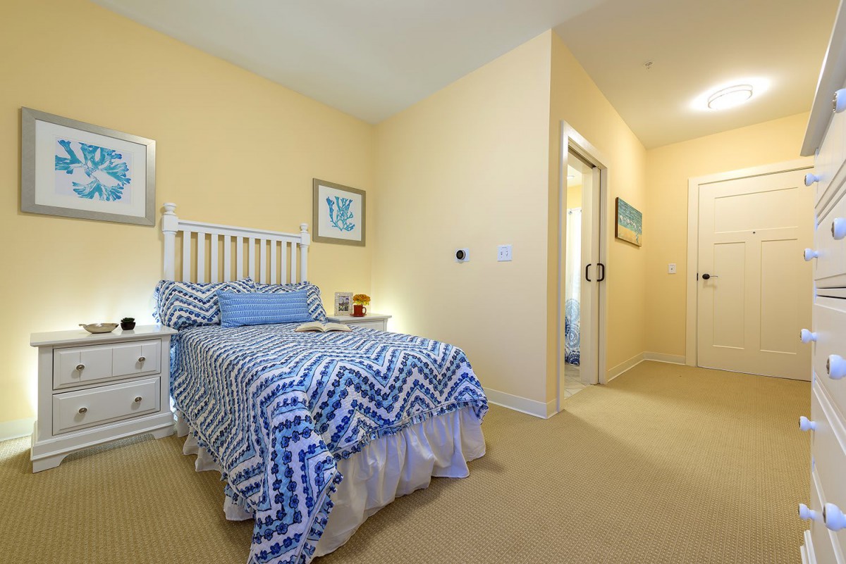 A cozy bedroom featuring a single bed with blue patterned bedding, complemented by a small nightstand and wall decor.