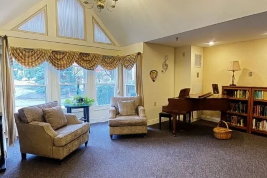 A cozy living room with plush chairs, a grand piano, and large windows adorned with elegant curtains.