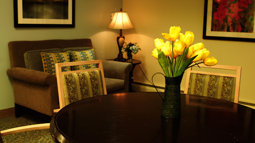 A cozy living room setting featuring a round table adorned with yellow flowers, complemented by a soft lamp and comfortable seating.