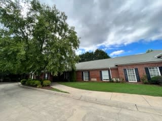 A brick building with a tree and well-maintained lawn under a cloudy sky.