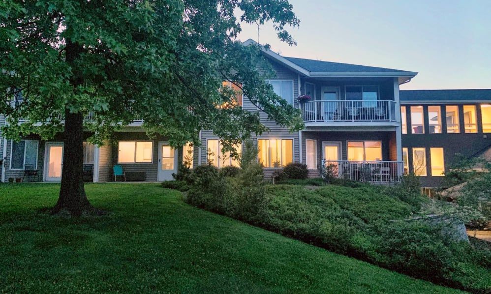 A two-story house with illuminated windows, surrounded by a well-maintained garden and lawn during the evening.