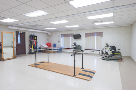 A spacious physical therapy room featuring balance bars and various exercise equipment.