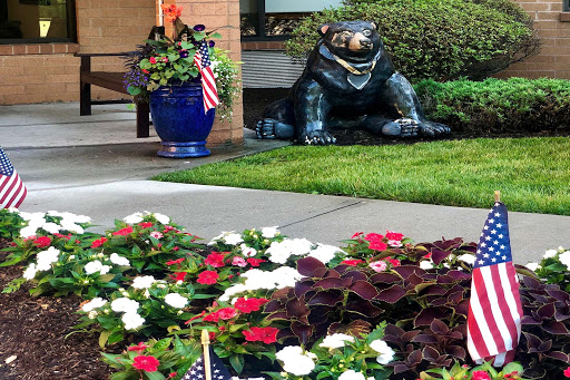 A charming garden scene featuring colorful flowers, a bear statue, and decorative planters.