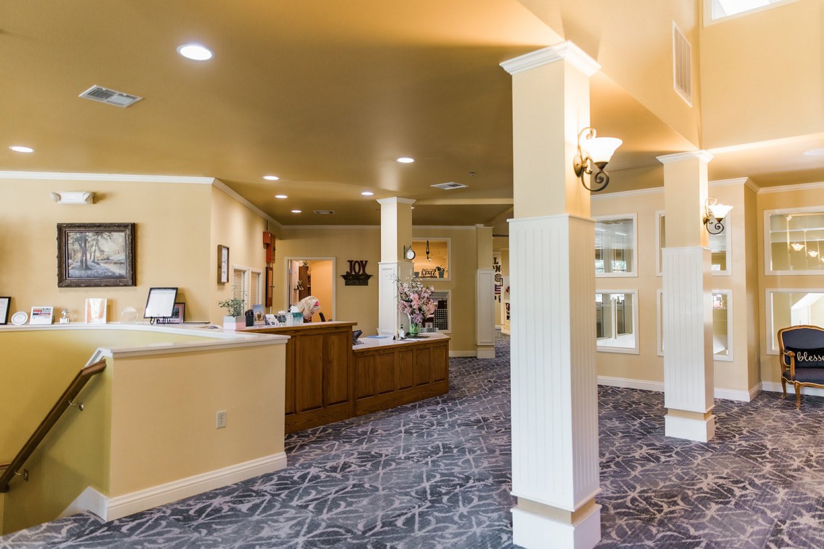 A spacious and well-lit lobby with a reception desk, columns, and carpet flooring.